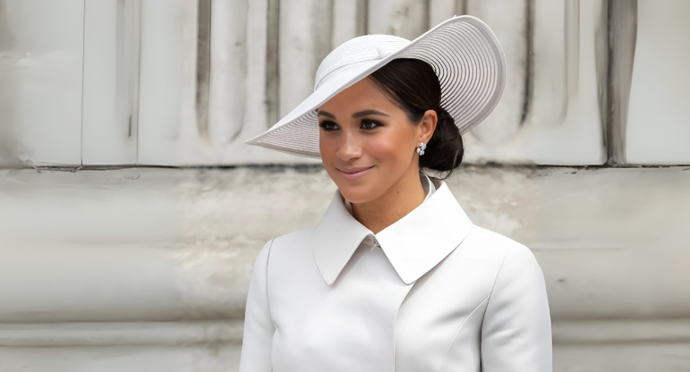 Royal Brothers Shatter Peace In Fight Over Diana’s Gems 2 Meghan Markle smiling in a white high-collared coat and wide-brimmed hat.